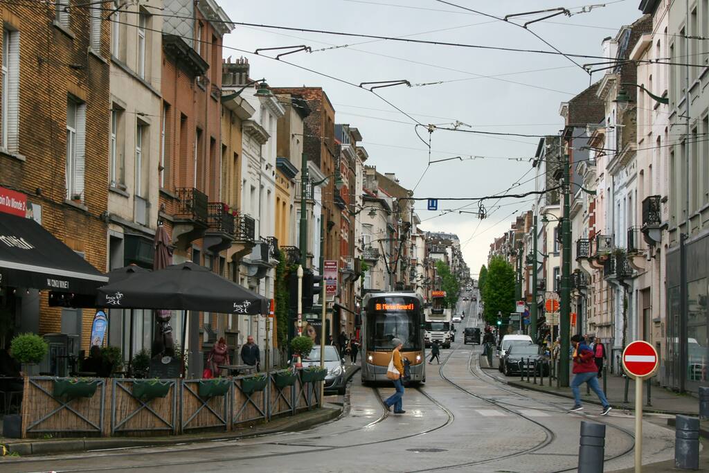 Rue bruxelloise bordée de maisons en briques, avec un tram et une terrasse de café.