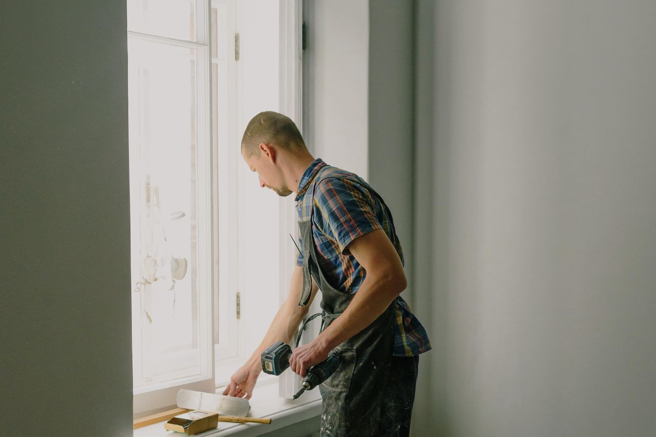 Artisan en rénovation intérieure, perceuse en main, près d’une fenêtre.