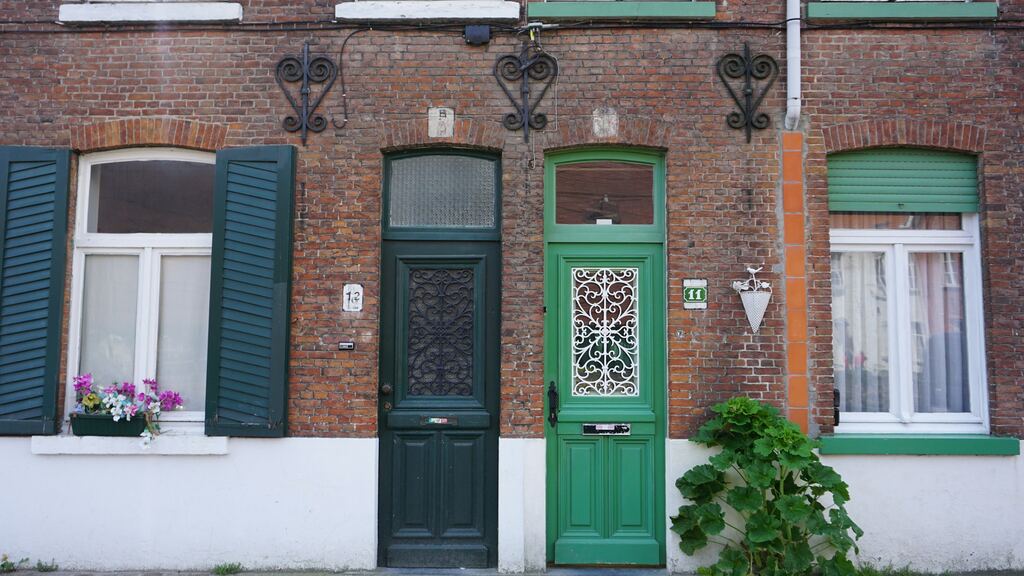 Deux maisons de rangée mitoyennes en briques, portes d’entrée vertes sous des linteaux cintrés.