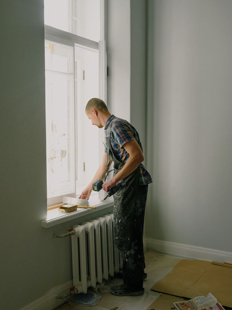 Artisan en rénovation intérieure, perceuse en main, près d’une fenêtre.